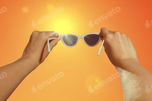 Preview: Woman holding sunglasses against orange sky with bright sun, closeup