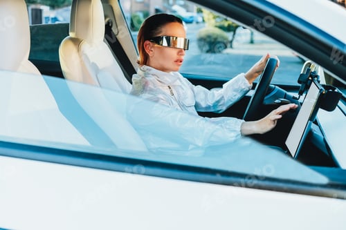 Preview: Fashion girl driving a white supercar. Red hair woman with futuristic eyeglasses sits by car wheel
