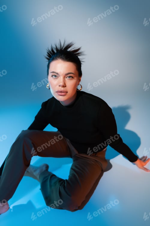 Preview: young brunette woman in black sweater looking at camera while posing on blue background