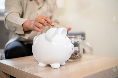 Preview: Close up office worker man putting coin in piggy bank aside glass jar sitting on sofa in living room