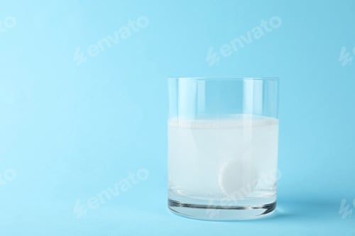 Preview: Glass of water with effervescent tablet on light blue background, space for text