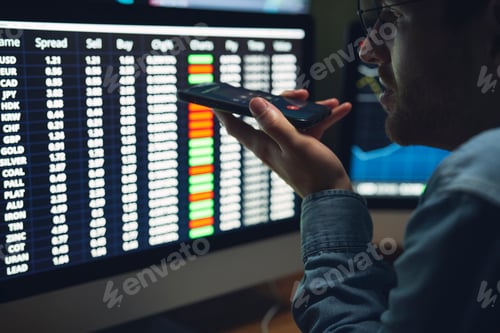 Preview: Young man talking on mobile phone and working on computer at home office at night