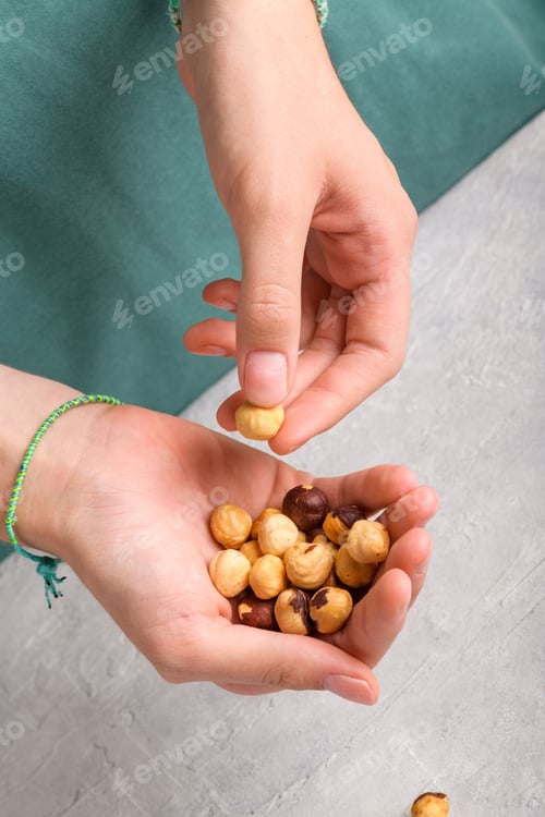Preview: Woman holding peeled whole hazelnuts in her hands at gray table, closeup.