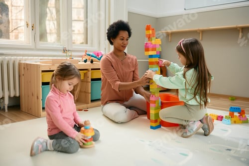 Preview: Happy black teacher and preschool kids playing with toy blocks in a playroom.