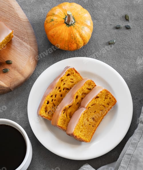 Preview: Pumpkin sweet bread or cake with icing on a plate on a dark background with decorative pumpkins