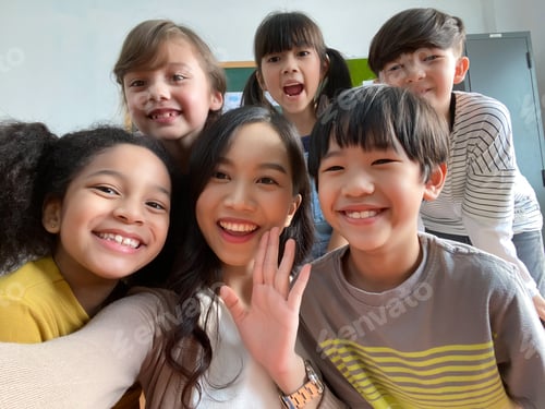 Preview: Smiling young Asian teacher making selfie with her schoolchildren in classroom.