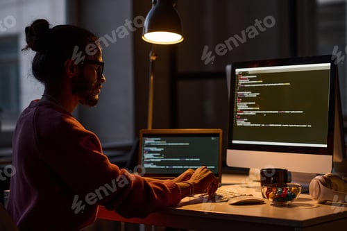 Preview: Young programmer sitting at his workplace and working on computer with codes, he working in office