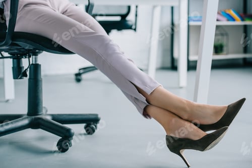 Preview: cropped shot of businesswoman in stylish high heeled shoes sitting at workplace