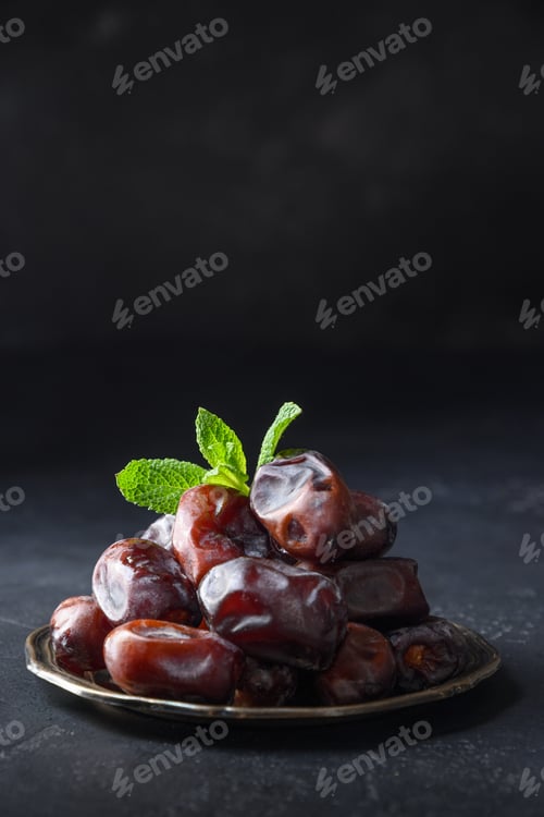 Preview: Ramadan. Iftar starts. Dates in bowl garnish mint on black background. Close up. Vertical format.