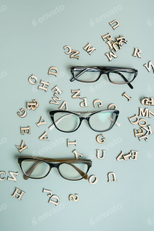 Preview: Eyeglasses on pastel green background with wooden letters. Vision test,optical store concept