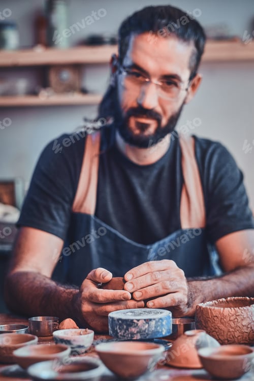 Vista previa: Un hombre diligente con gafas en su taller de cerámica está trabajando en un nuevo proyecto.