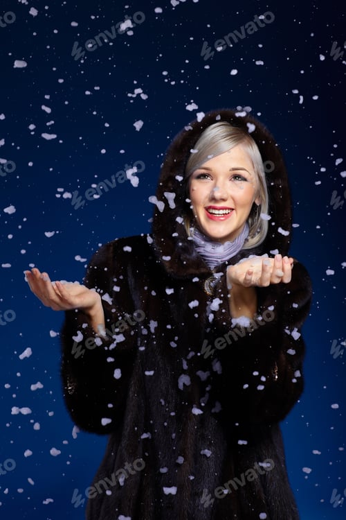 Preview: Beautiful European Blonde Woman In Fur Coat Smiling In Snow Flakes On Blue