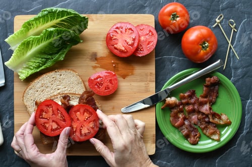 Preview: Making BLT sandwich - woman placing tomato slices on whole wheat bread with mayo bacon lettuce