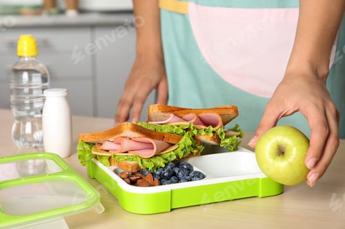 Preview: Woman preparing food for her child at table in kitchen, closeup. Healthy school lunch