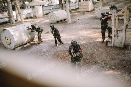 Preview: high angle view of paintball team in uniform and protective masks playing paintball with markers