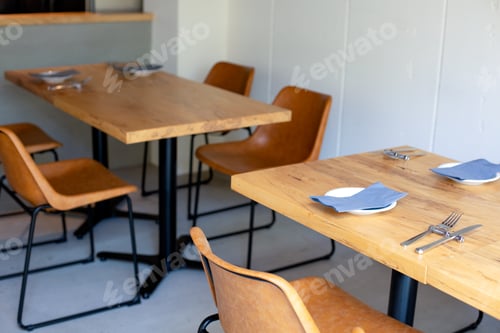 Preview: Tables and chairs in a restaurant, plain white walls and grey flooring, place settings.