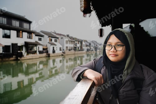 Preview: Portrait of a muslim girl wearing hijab sitting next to the small river near the ancient town,China.