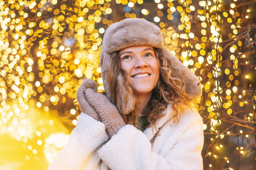 Preview: Young happy woman with curly hair in fur jacket having fun in winter street decorated with lights