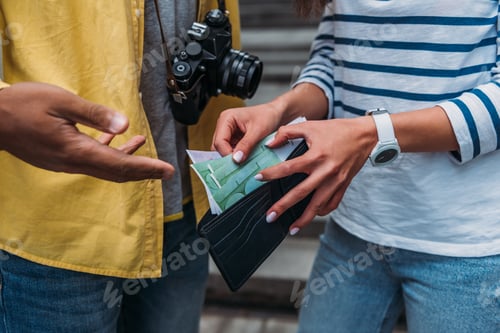 Preview: Cropped view of woman checking money in wallet near bi-racial friend