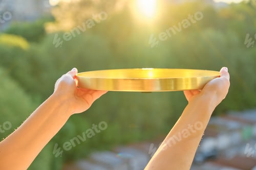 Preview: Round golden brass metal tray in womans hands, background sunset