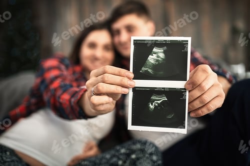 Preview: Happy and excited pregnant couple looking at the ultrasound images of their baby lying on the bed