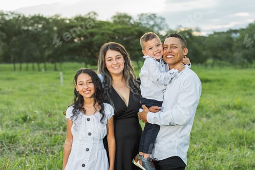 Preview: latin family posing happily in a green field, all four are smiling.