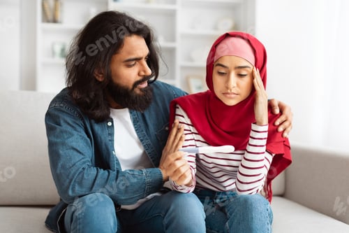 Preview: Concerned Man Comforting Distressed Woman in Hijab Indoors During Daytime