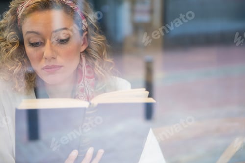 Preview: Beautiful woman reading book seen through cafe window