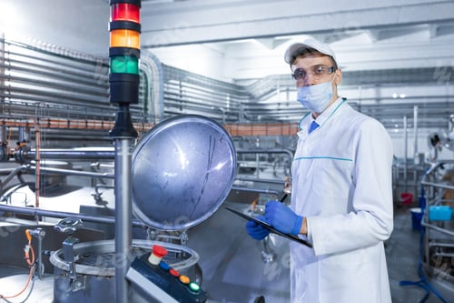Preview: Inspector in a mask and a scrub stands with a folder-tablet in his hands at the dairy plant