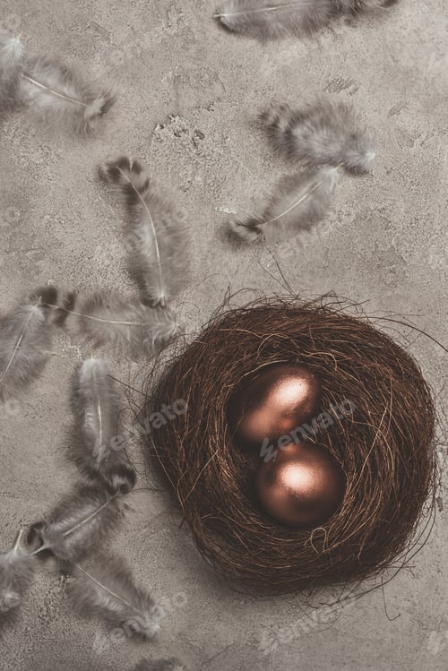 Preview: top view of golden easter eggs in nest with feathers on concrete surface