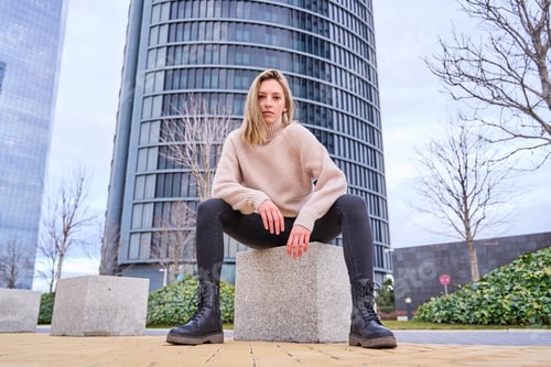 Preview: young woman in casual clothes sitting on a stone bench against a city backdrop