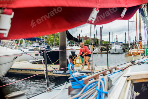Preview: Young woman on marina pier mooring sailboat looking at camera smiling