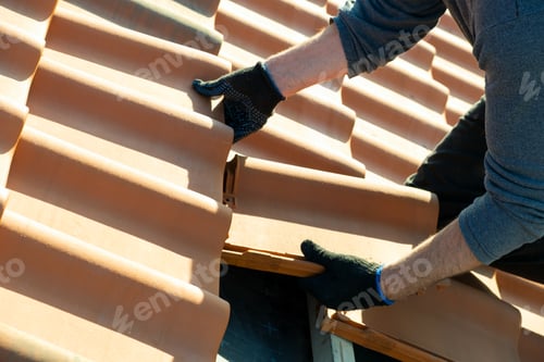 Preview: Closeup of worker hands installing yellow ceramic roofing tiles mounted on wooden boards covering