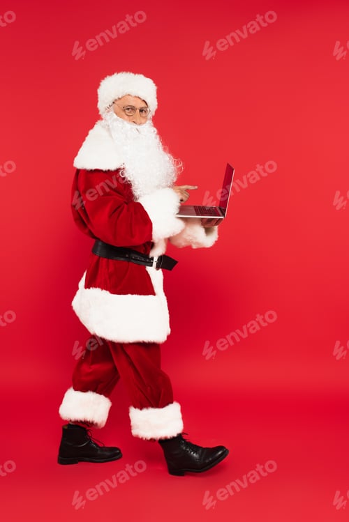 Preview: Santa claus pointing at laptop with blank screen on red background