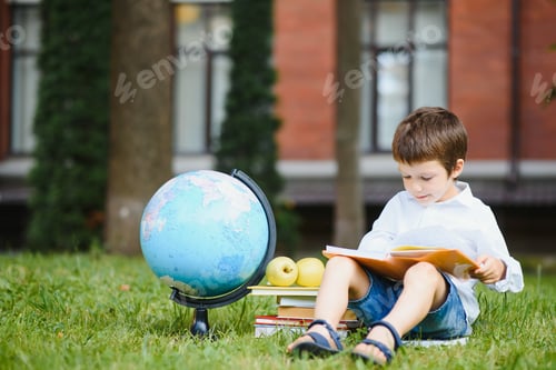 Preview: Pupil near school. Boy sitting with a book.
