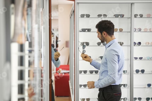 Preview: Man studying sunglasses in showroom of optician shop