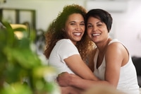 Preview: Smiling Women Embrace Indoors with Greenery Nearby
