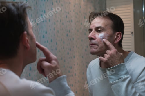 Preview: Senior man applying cream to face at bathroom