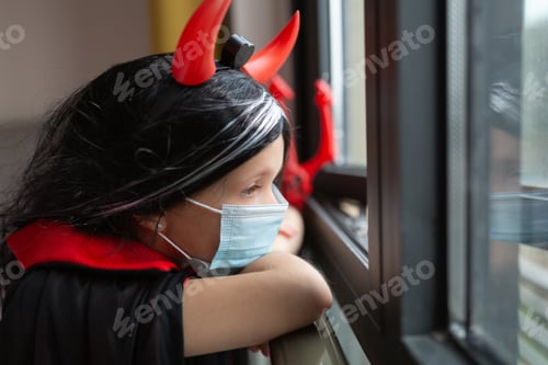 Preview: Little caucasian girl six years old in evil costume and mask celebrates Halloween during coronavirus