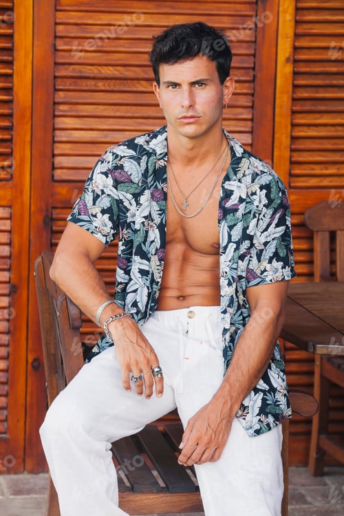 Preview: Serious young man in stylish summer outfit sitting on chair