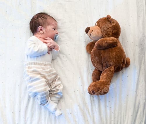 Preview: Cute little baby laying with his teddy bear on bed