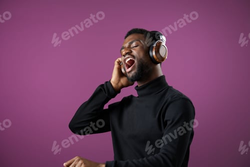 Preview: Young Black man singing joyfully with headphones against a vibrant purple background, showcasing