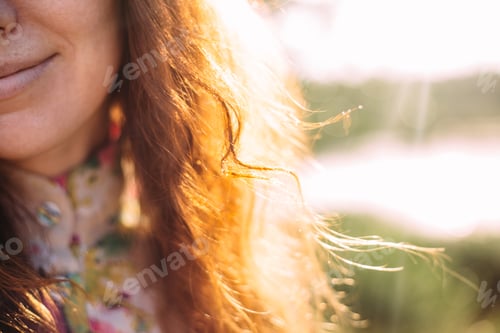 Preview: Portrait of a beautiful red-haired girl with curls smiling resting in nature. Sun rays in red hair