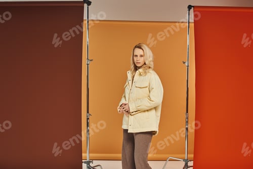 Preview: fall fashion, attractive woman in autumn attire looking at camera and posing on orange backdrop