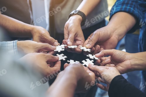 Preview: Closeup image of many people hands holding a jigsaw puzzle in circle together