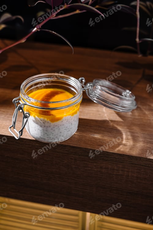 Preview: Chia pudding with mango puree in glass jar on wooden table is waiting for client of cafe