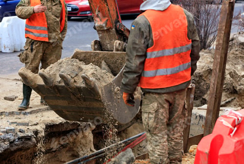 Preview: Bucket of a heavy construction excavator surrounded by road workers lifts sand during a sewer repair