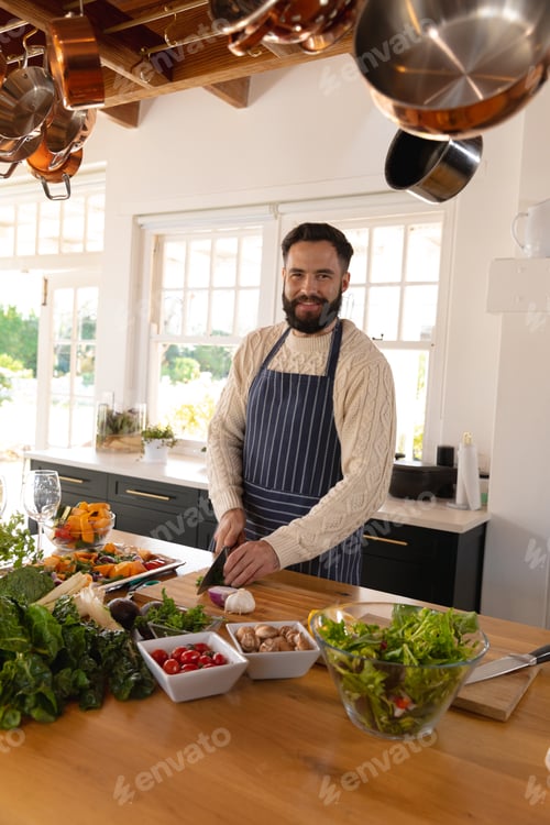 Preview: Portrait of happy caucasian man with beard chopping vegetables wearing apron in kitchen
