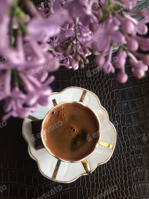 Preview: Top view of a cup of a coffee on a leather table and purple flower