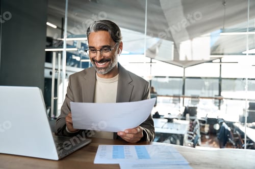 Preview: Happy middle aged business man looking at laptop hybrid working in office.